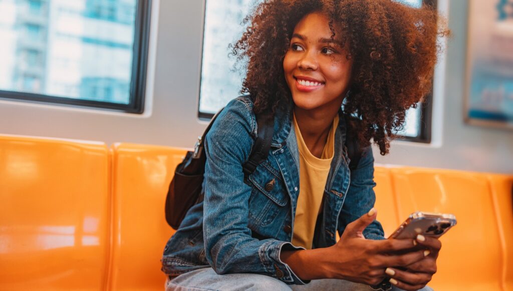 Happy, smiling student travelling by train using her digital device.