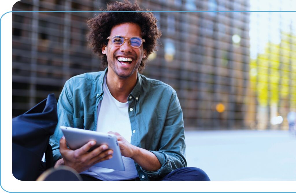 Smiling man using a tablet device to record curriculum data in front of a university building on a sunny day.