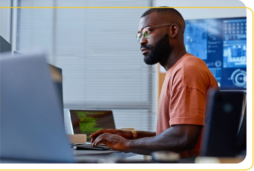 Young black man sitting at a desk surrounded by tech and monitors