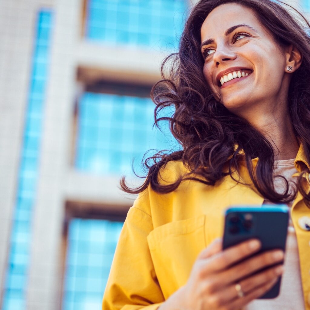 Smiling woman holding coffee cup while accessing curriculum management platform on mobile device.