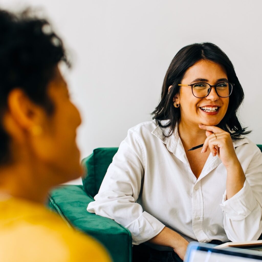 Two smiling women sitting using digital devices in a curriculum review meeting